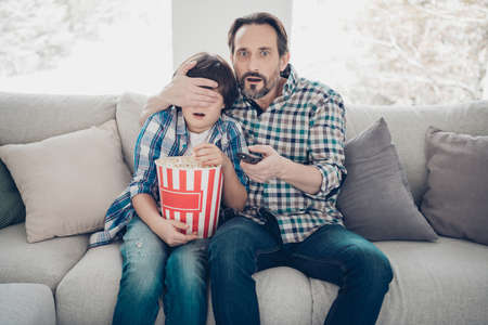 Its forbidden for little kids to watch this program concept. Photo of excited shocked amazed surprised mature daddy closing eyes to his offspring changing channelの写真素材