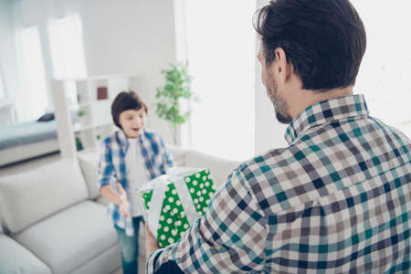 Rear back behind view portrait of two nice attractive cheerful cheery glad guys dad daddy giving gift purchase box to pre-teen son event in light white modern interior house living-room indoorsの写真素材