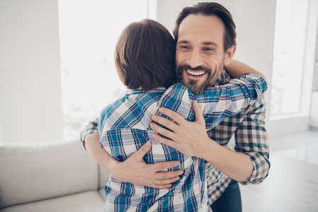 Close-up portrait of two nice attractive lovely cheerful cheery guys dad and pre-teen son meeting day hugging in light white modern style interior house living-roomの写真素材