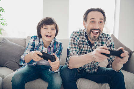 Portrait of two nice attractive cheerful cheery glad guys dad and pre-teen son spending day playing online video game at light white modern style interior house living-room indoorsの写真素材