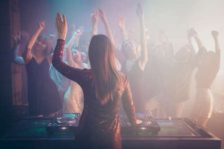 Rear back behind view of dj performing stereo sound rhythm trance techno, electronic style music for stylish cheery crowd enjoying event concert having fun bachelor at fashionable modern nightclubの写真素材