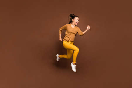 Full length body size photo of cheerful sweet pretty cute nice charming girl urgent for sales and discounted goods wearing yellow pants trousers isolated over brown pastel color backgroundの写真素材