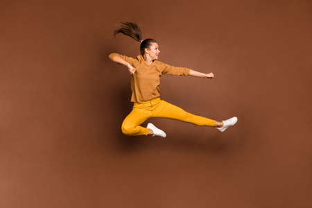 Full length body size photo of cheerful nice cute attractive girl practicing her fighting skills kicking empty space with foot jumping up isolated over brown pastel color backgroundの写真素材