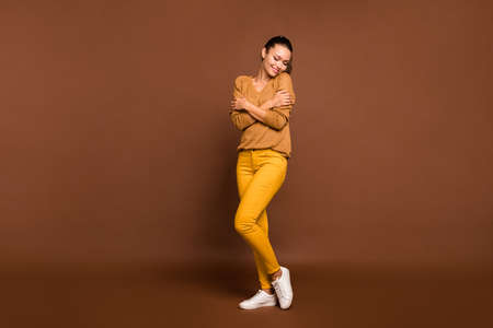 Full length body sizep photo of cheerful cute positive charming sweet girlfriend embracing herself warmened with sweater with her eyes closed isolated over brown pastel color backgroundの写真素材