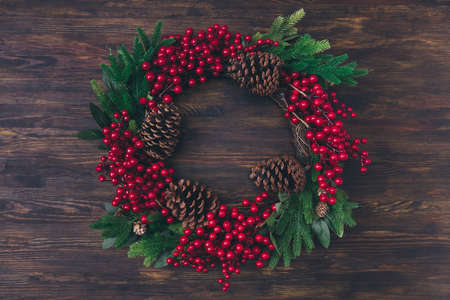 Top above high angle view photo of winter christmas traditional seasonal wreath with green fir tree leaves pine cone red mistletoe berries lay on brown wooden table isolatedの写真素材