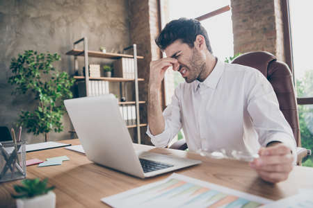 Profile side photo of tired middle eastern entrepreneur man have much work on laptop try concentrate touch his nose hold glasses sit desk in loft workplaceの写真素材