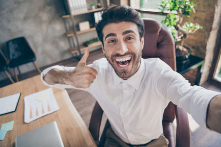 Great partnership online meeting. Close up photo of positive cheerful middle eastern entrepreneur make selfie show thumb up approve his new work clients sit chair in loft workstationの写真素材