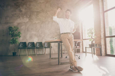 Full size photo of ecstatic indian freelancer having glasses feeling smart get sms about new partners start-up deal scream yes raise fists wear white shirt pants trousers stand in loft workplaceの写真素材