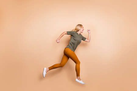 Full length profile photo of crazy lady jumping high speed race marathon participant competitive mood rushing sales wear green t-shirt yellow trousers isolated beige color backgroundの写真素材