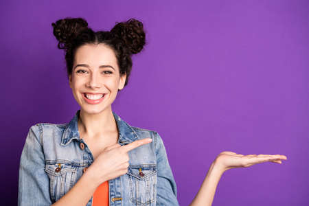 Close up photo of positive cheerful girl promoter hold hand point index finger present demonstrate promotion ads wear stylish trendy outfit isolated over bright color backgroundの写真素材