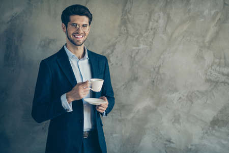 Portrait of positive attractive guy rich wealthy entrepreneur have rest relax hold cup with americano coffee feel peaceful on his workplace wear modern outfit isolated over grey color backgroundの写真素材