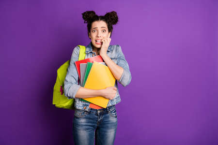 Portrait of frustrated scared high school girl hear news session exam nail bite feel fear hold notebooks wear stylish trendy denim jeans jacket green backpack isolated bright purple color backgroundの写真素材