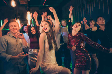 Photo of big company of students having entered night club to have fun and dance together with excited facial expressions and lights shining aboveの写真素材