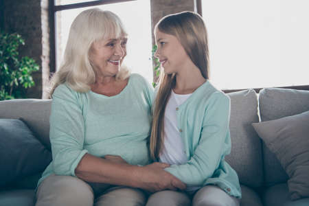 I havent seen you for ages. Photo of two people cute aged granny and granddaughter sit cozy sofa hug...