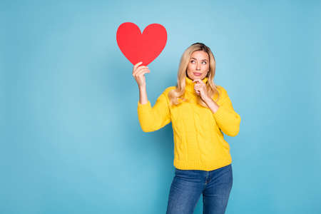 Photo of amazing blond lady holding big red paper heart thinking over right answer on date...