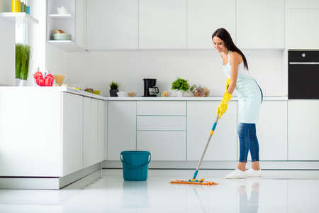 Profile side full size photo of positive cheerful girl having mop washing floor wearing white singlet yellow rubber gloves dotted apron fell content enjoy household chores in kitchen house indoorsの写真素材