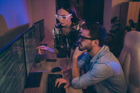 Profile photo of it specialist two serious guy lady business people night coworking watch direct monitors errors bugs writing interface back-end code office indoorsの写真素材