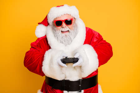 Portrait of funny funky crazy santa claus play videogame on newyear holly noel celebration have excited entertainment isolated over yellow color backgroundの写真素材