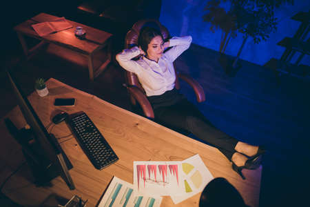 Top above high angle view of nice attractive stylish chic peaceful calm lady top executive manager lawyer attorney finance company agency owner resting legs on desktop at night dark work place stationの写真素材