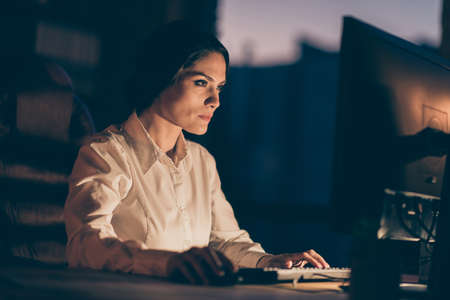 Close-up profile side view portrait of her she nice attractive lovely focused concentrated smart clever busy lady creative designer copywriter typing creating design at night dark work place stationの写真素材