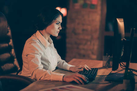 Profile side view portrait of her she nice attractive concentrated smart clever busy lady hardworking typing creating new finance management strategy plan at night dark work place stationの写真素材