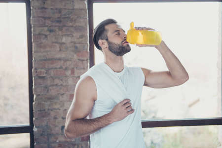 Photo of handsome sportsman guy finished morning training drinking fresh water holding towel eyes...