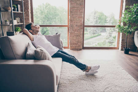 Profile photo of mixed race guy sitting cozy sofa holding hands behind head relaxing homey weekend...