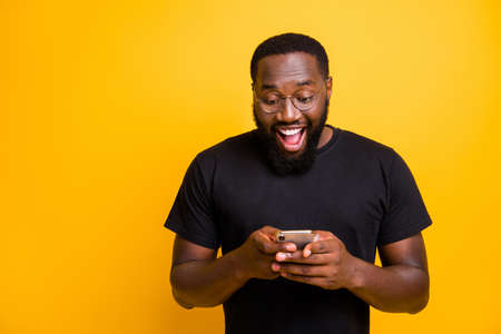 Photo of toothy mixed-race, handsome funny man brunet haired in t-shirt overjoyed about receiving positive notification of feedback isolated vivid yellow color backgroundの写真素材