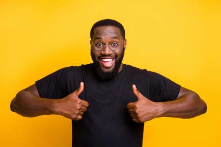 Photo of cheerful positive, attractive man smiling toothily showing two thumbs up in t-shirt with brown hair isolated vivid color backgroundの写真素材