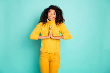 Photo of cute dark skin wavy lady holding hands together asking to buy, candy wear yellow knitted pullover stylish pants isolated blue teal color backgroundの写真素材