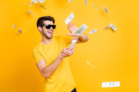 Photo of young handsome careless guy throwing money banknotes away wealthy person wear sun specs casual t-shirt isolated bright yellow color backgroundの写真素材