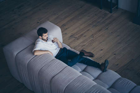 Top above high angle view of his he nice attractive serious imposing guy lying on divan drinking beverage having rest free spare time at modern industrial loft interior open space work place stationの写真素材