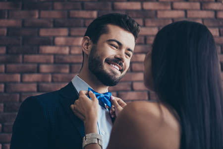 Closeup photo of two affectionate people couple guy looking eyes lady who fixing, blue stylish bow tie best pair at prom wear classy formalwear suit dress loft indoorsの写真素材
