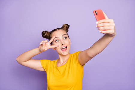 Photo of cheerful positive cute nice charming sweet funny girl showing v-sign taking selfie holding...
