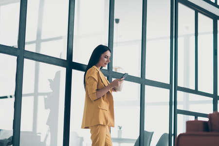 Profile side view portrait of her she nice attractive charming pretty classy lady drinking aromatic coffee using digital device in modern style light white high glass interior apartment houseの写真素材
