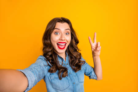 Photo of cute curly wavy cheerful girlfirend showing you v-sign smiling toothily while taking selfie...