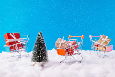 Christmas discounts concept. Photo of three santa claus unusual metal trolleys loaded giftboxes new transportation idea service newyear winter snowy colorful backgroundの写真素材
