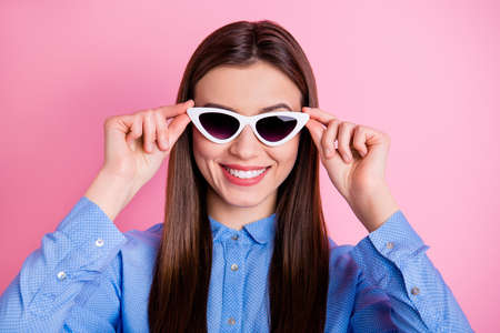 Close up photo of cute nice fascinating good lady wearing sunglass eyewear holding them with hands smiling toothily isolated over pink pastel color backgroundの写真素材