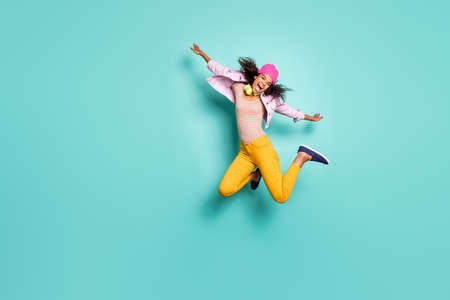 Full length body size photo of casual cheerful pretty nice free girlfriend wearing yellow trousers striped t-shirt pink cap headwear jacket flying jumping like air plane isolated teal vivid color backgroundの写真素材