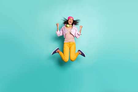 Full length body size side profile photo of casual positive jumping running school girl aspiring to come to educational complex on time in yellow pants pink jacket t-shirt isolated vivid color teal backgroundの写真素材