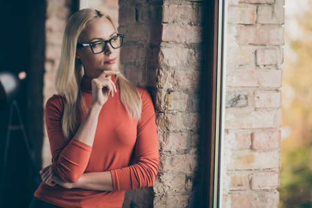 Profiel side photo of pensive minded entrepreneur charming woman stand look window think thoughts about start-up choice decide decision wear red turtleneck in office loftの写真素材