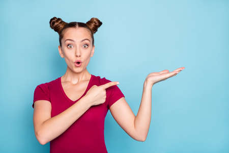 Photo of crazy excited cheerful stupor girlfriend holding empty space on her hand pointing at it with forefinger in red t-shirt lips pouted isolated over pastel color backgroundの写真素材