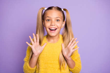 Portrait of positive cheerful kid hear wonderful news about her birthday newyear present scream wow omg raise hands wear yellow pullover isolated over purple color backgroundの写真素材