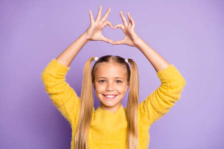 Photo of casual cheerful cute funny girl showing heart shape sign with fingers above her head isolated pastel violet color backgroundの写真素材