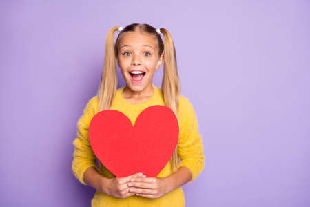 14-february omg. Portrait of cute impressed kid get hold big red paper card heart wonder scream wow unbelievable wear yellow jumper isolated over purple color backgroundの写真素材