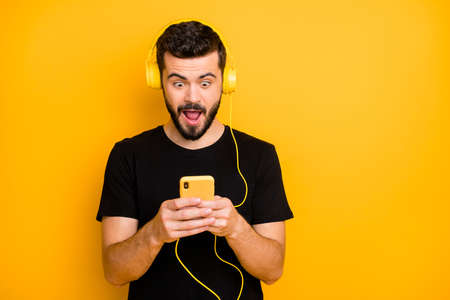 Omg super hit. Amazed surprised guy listen music use headset search sound track on his smartphone find unbelievable song scream wear good looking outfit isolated over yellow backgroundの写真素材