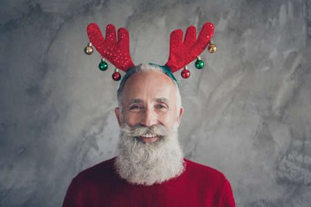 Portrait of positive stylish old man hipster in deer headband enjoy christmas party x-mas celebration wear red modern pullover isolated over grey concrete wall color backgroundの写真素材