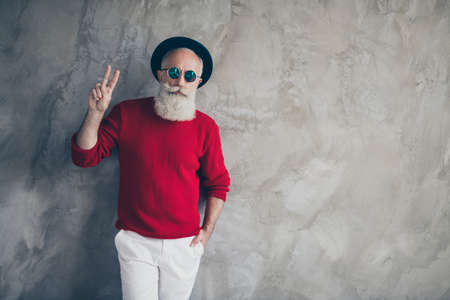 Portrait of stunning serious white grey hair beard old man celebrate x-mas christmas time make v-sign wear fashion luxury pullover pants isolated grey concrete wall color backgroundの写真素材