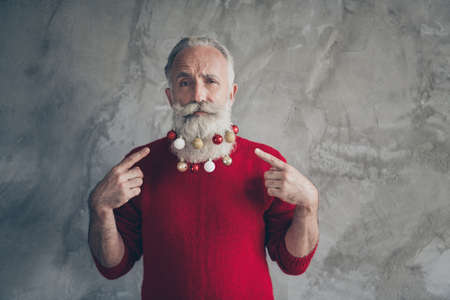 Portrait of serious masculine cool old man point index finger on christmas tree toy hang on his...