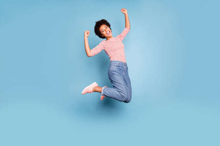 Full body photo of excited enthusiastic afro american girl jump show her triceps wear striped shirt...